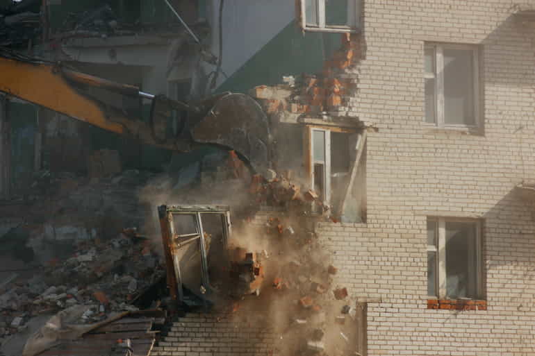 Demolizione di un edificio civile effettuata tramite il braccio meccanico di un escavatore